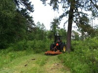A tractor driving down a trail, mowing the vegetation on the trail.